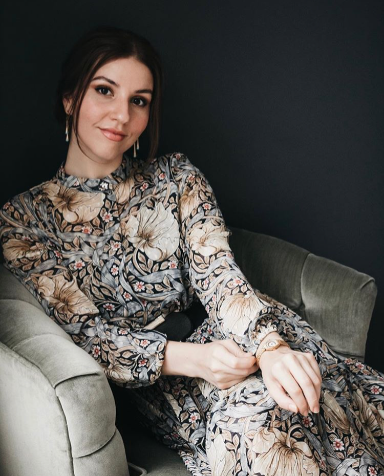 Author of lifestyle blog wearing floral dress sitting on velvet chair.